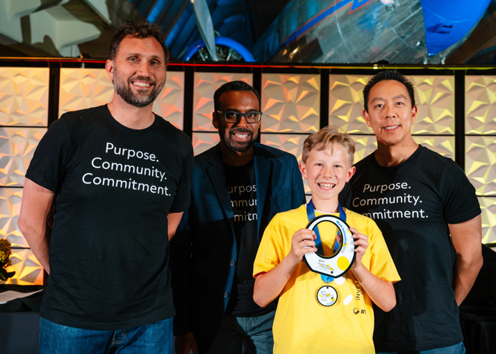 most innovative 2026 A boy in a yellow shirt poses with a white trophy award in front of three men